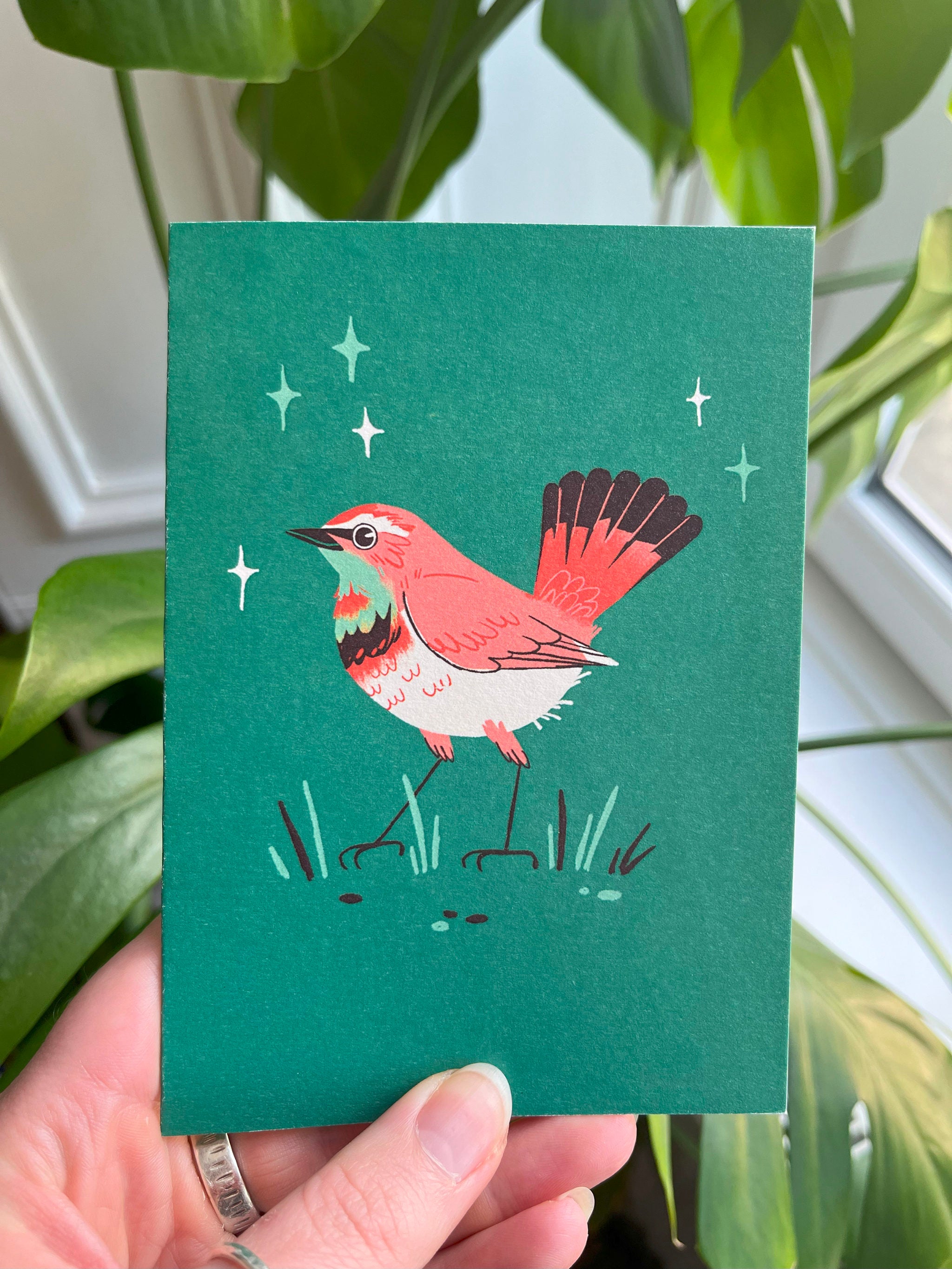 Bluethroat greetings card -- card with a red bird illustration held in front of green plants.