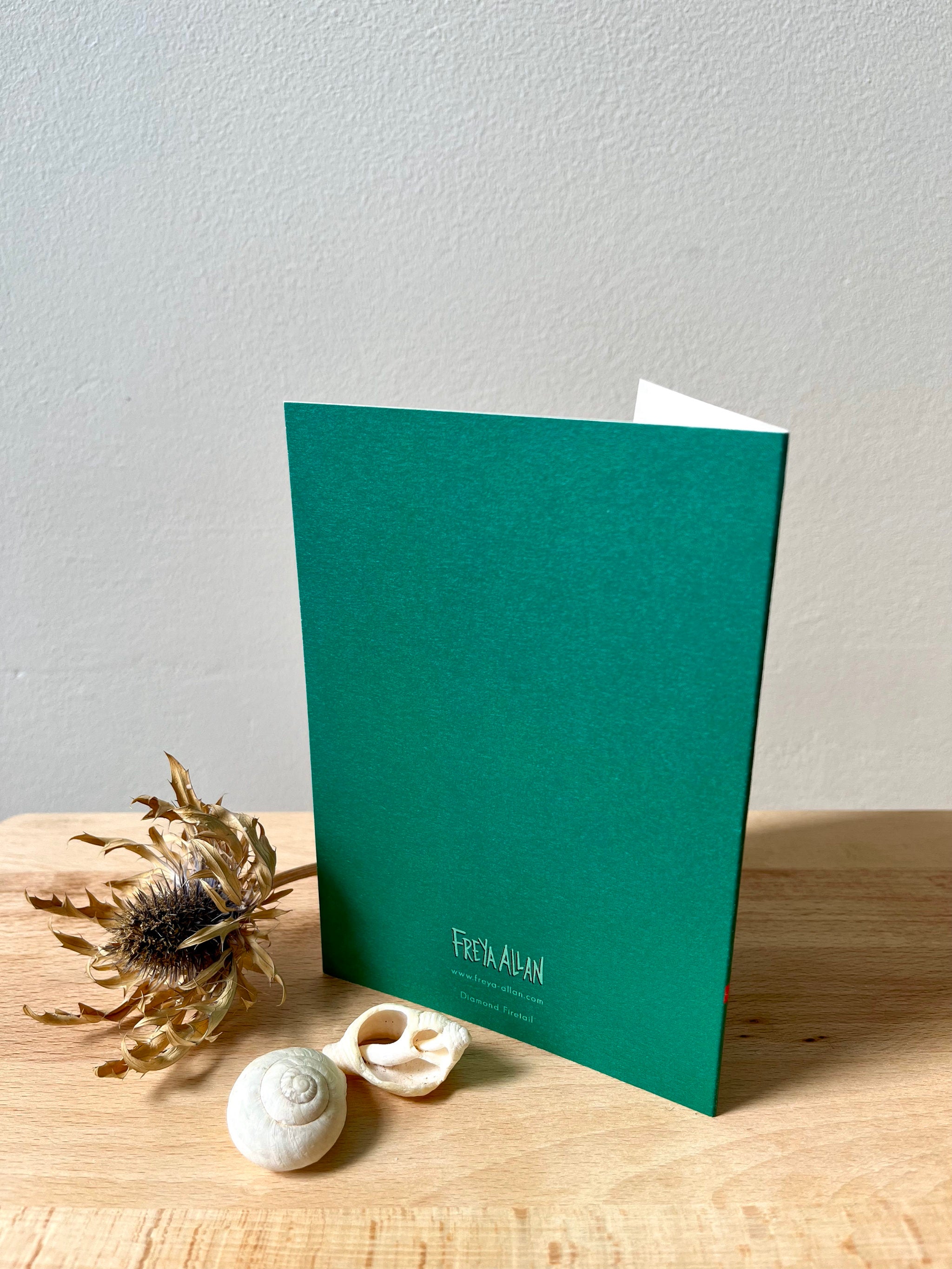 Diamond Firetail greetings card -- teal greeting card with 'Freya Allan' branding on a wooden surface with decorative elements.