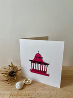 Dundee Bandstand greetings card -- greeting card with a red pagoda design on a wooden surface with seashells and a dried plant.