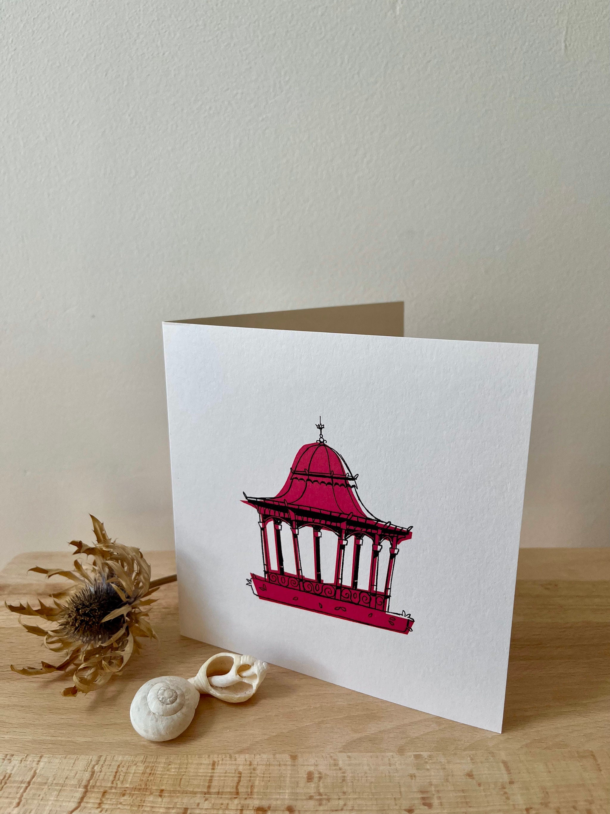 Dundee Bandstand greetings card -- greeting card with a red pagoda design on a wooden surface with seashells and a dried plant.