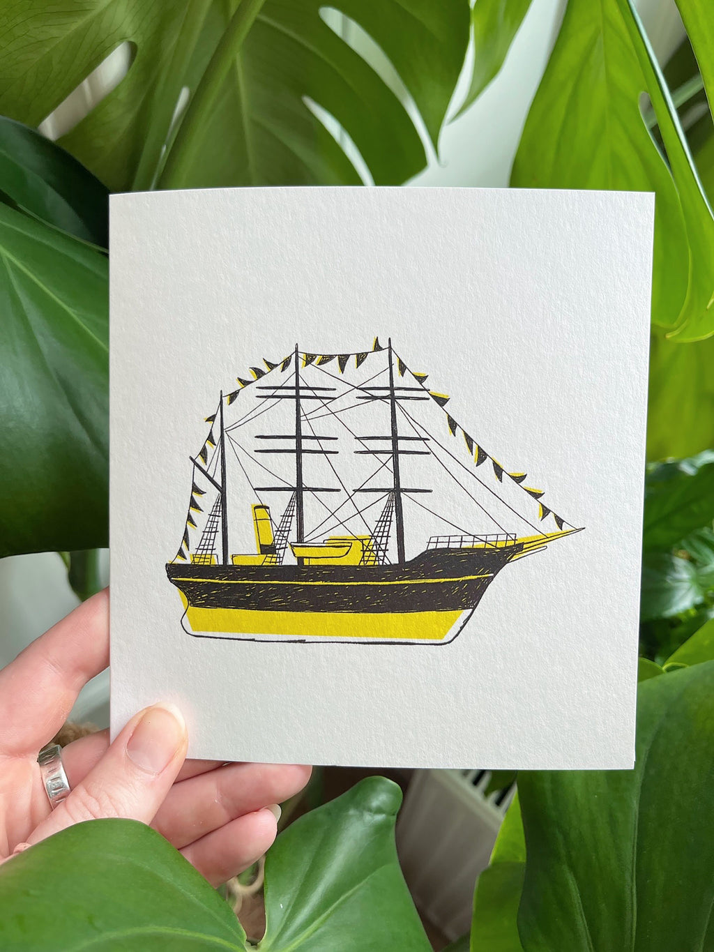 Discovery greetings card -- hand holding a card with a ship illustration against a green leafy background
