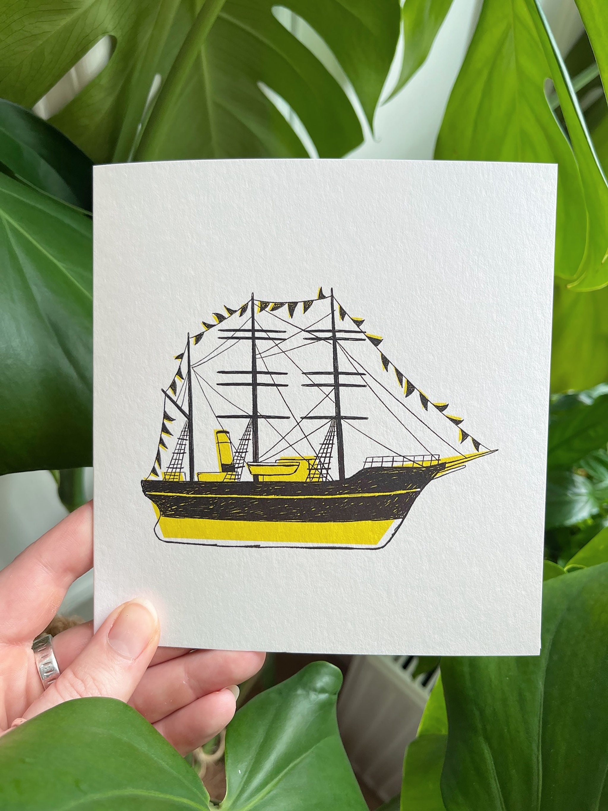 Discovery greetings card -- hand holding a card with a ship illustration against a green leafy background