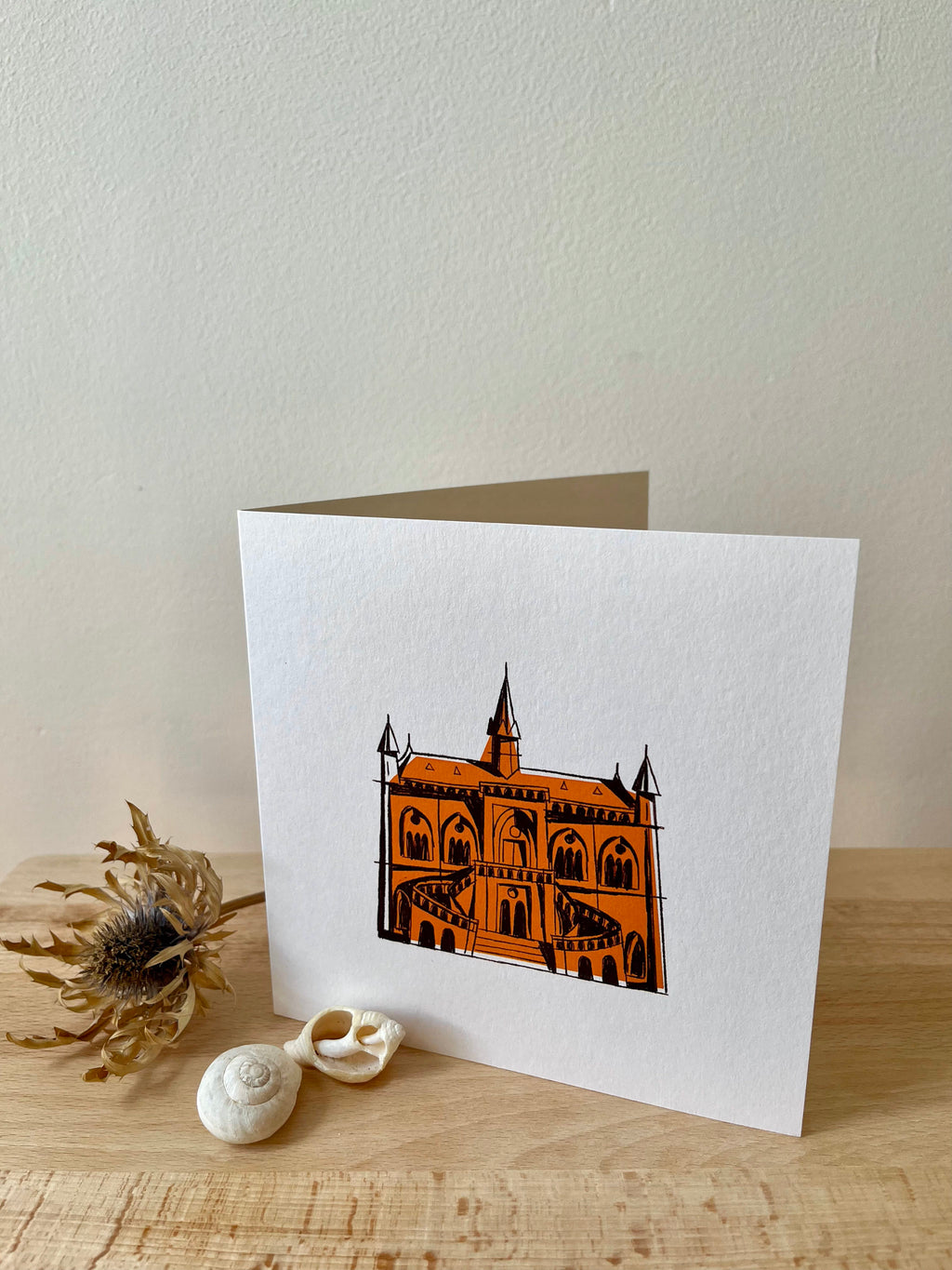 McManus Gallery greeting card -- greeting card with a 'castle' illustration on a wooden surface with seashells and a dried plant.