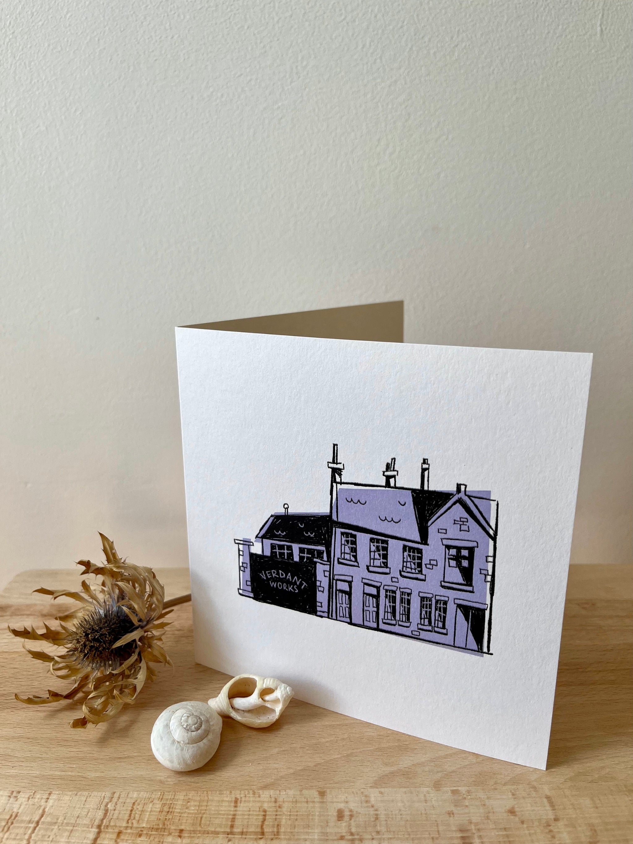 Verdant Works greetings card -- greeting card with a house illustration on a wooden surface with decorative elements.