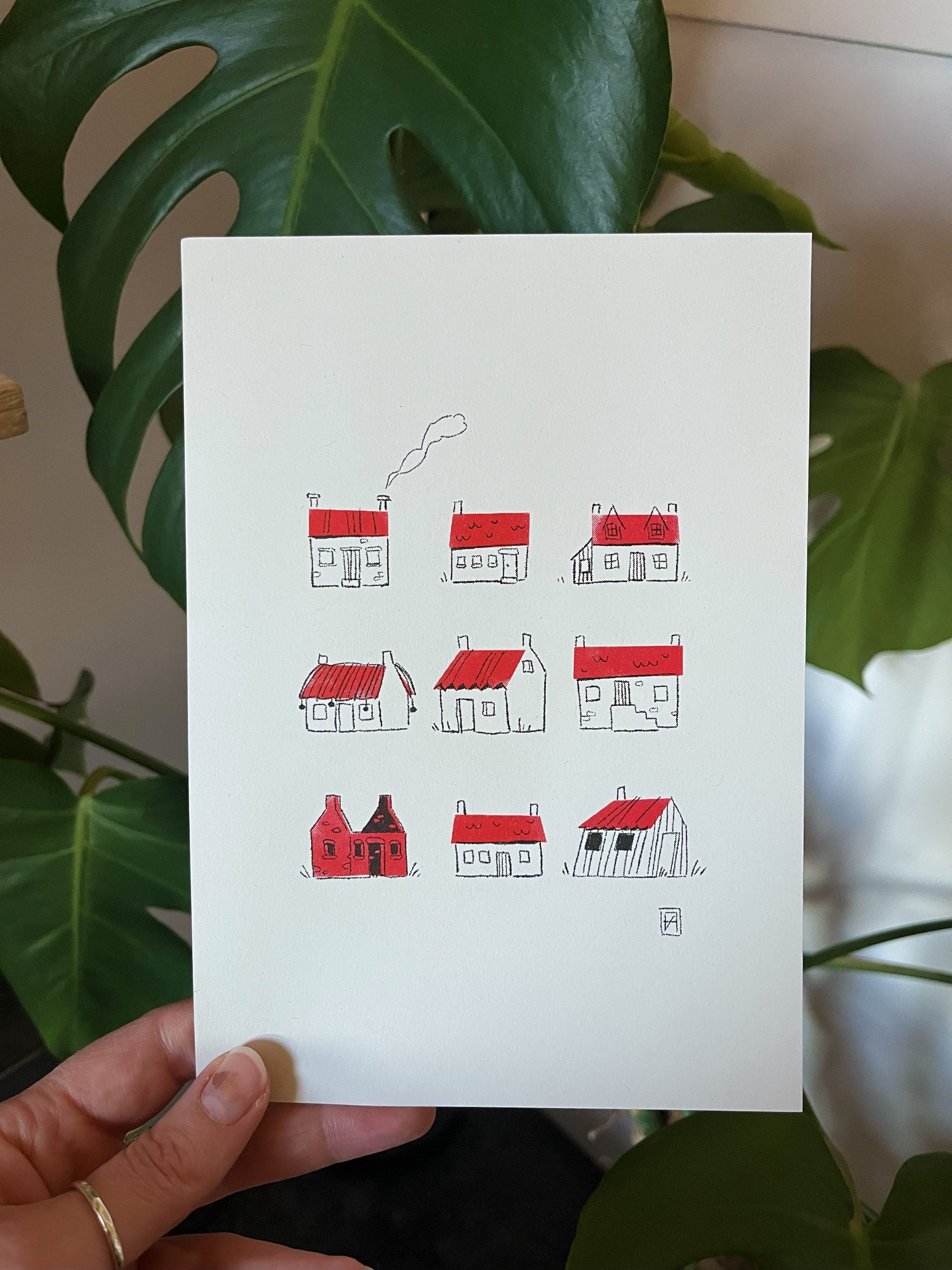 Couthie Bothies greetings card --  with red and white house illustrations held by a hand against a leafy background.