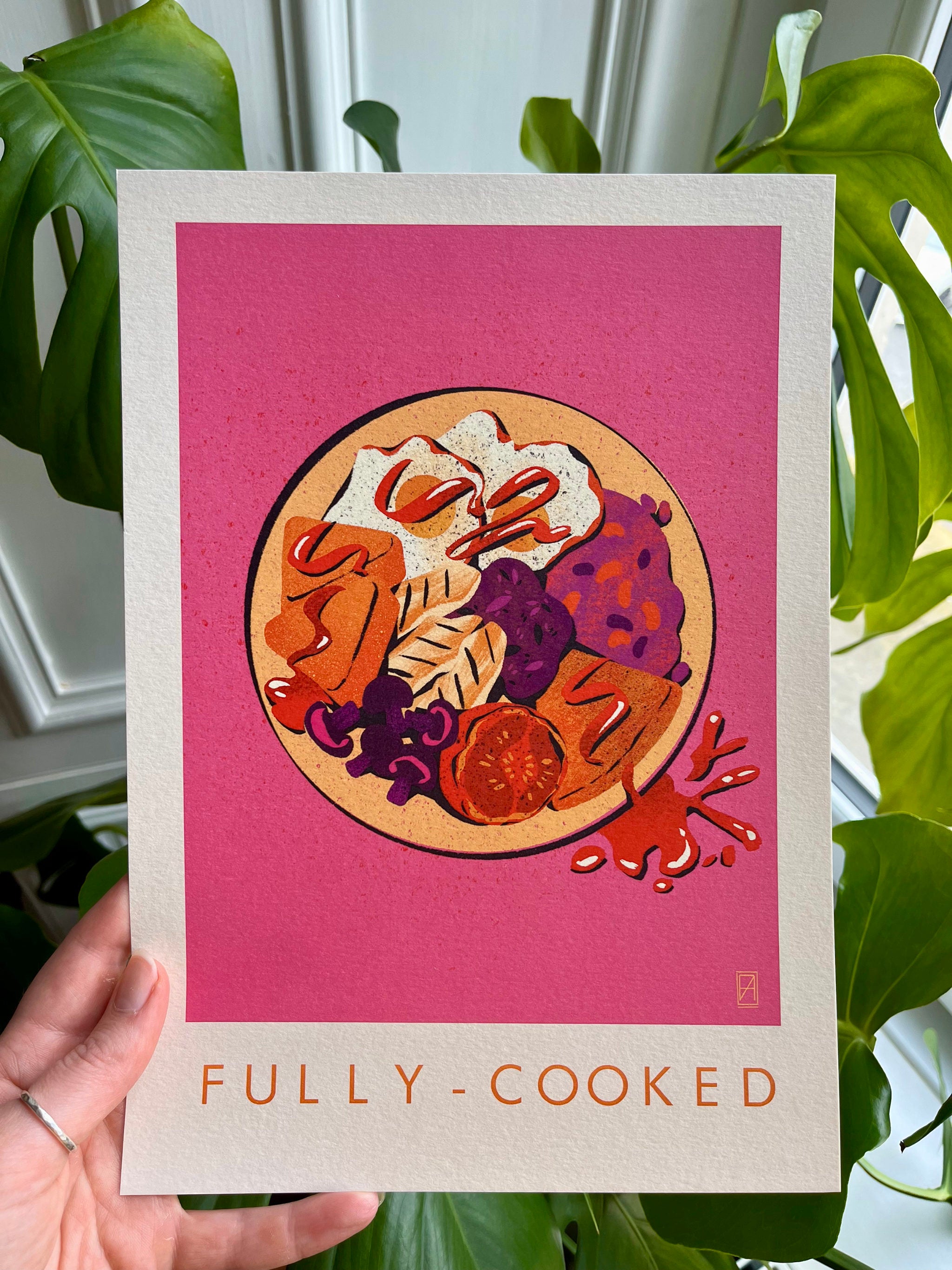 Fully Cooked print -- A4 print with food illustration on a pink background held by a hand with green leaves in the background.