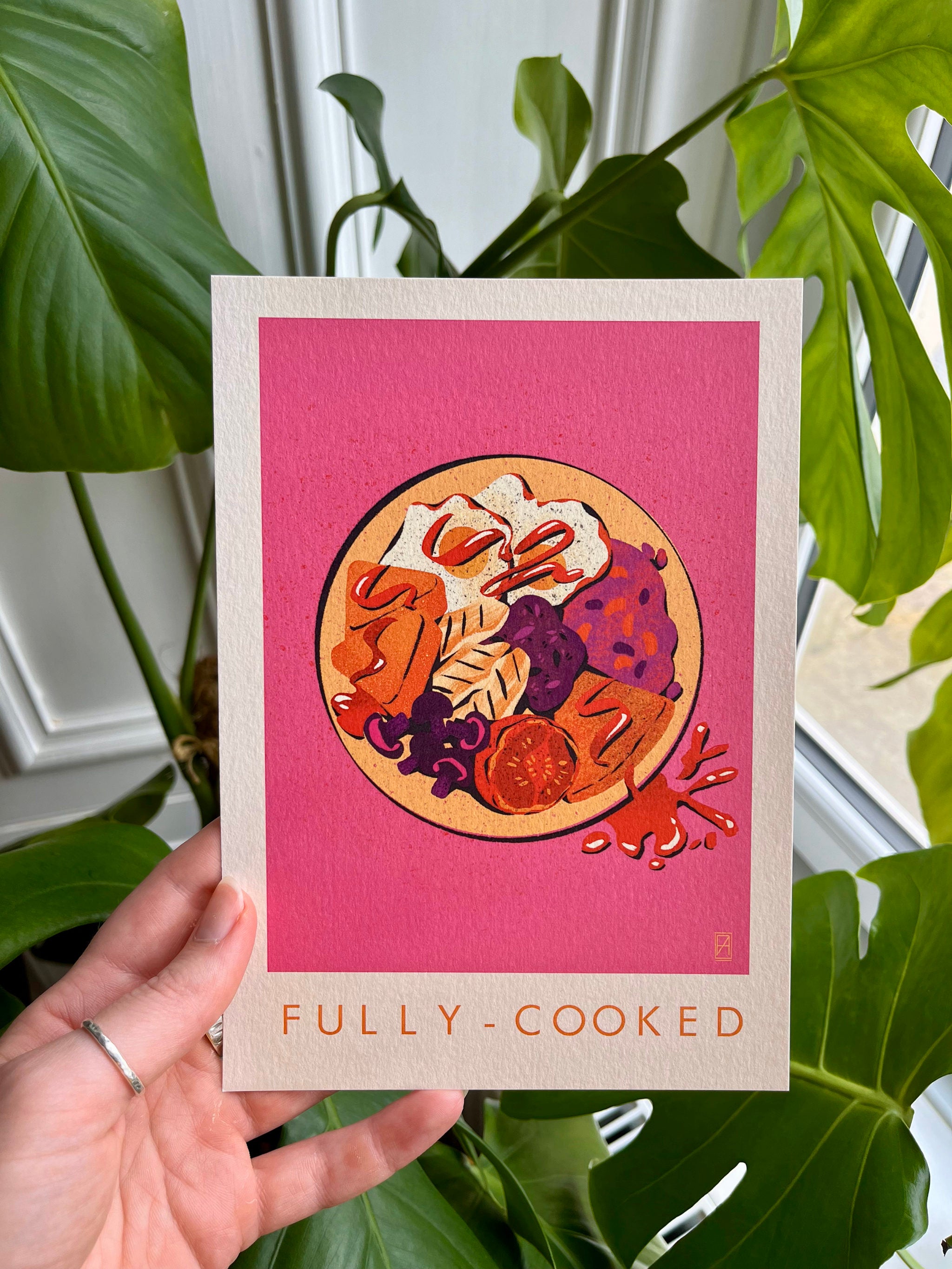 Fully Cooked print -- A5 print with food illustration on a pink background held by a hand with green leaves in the background.