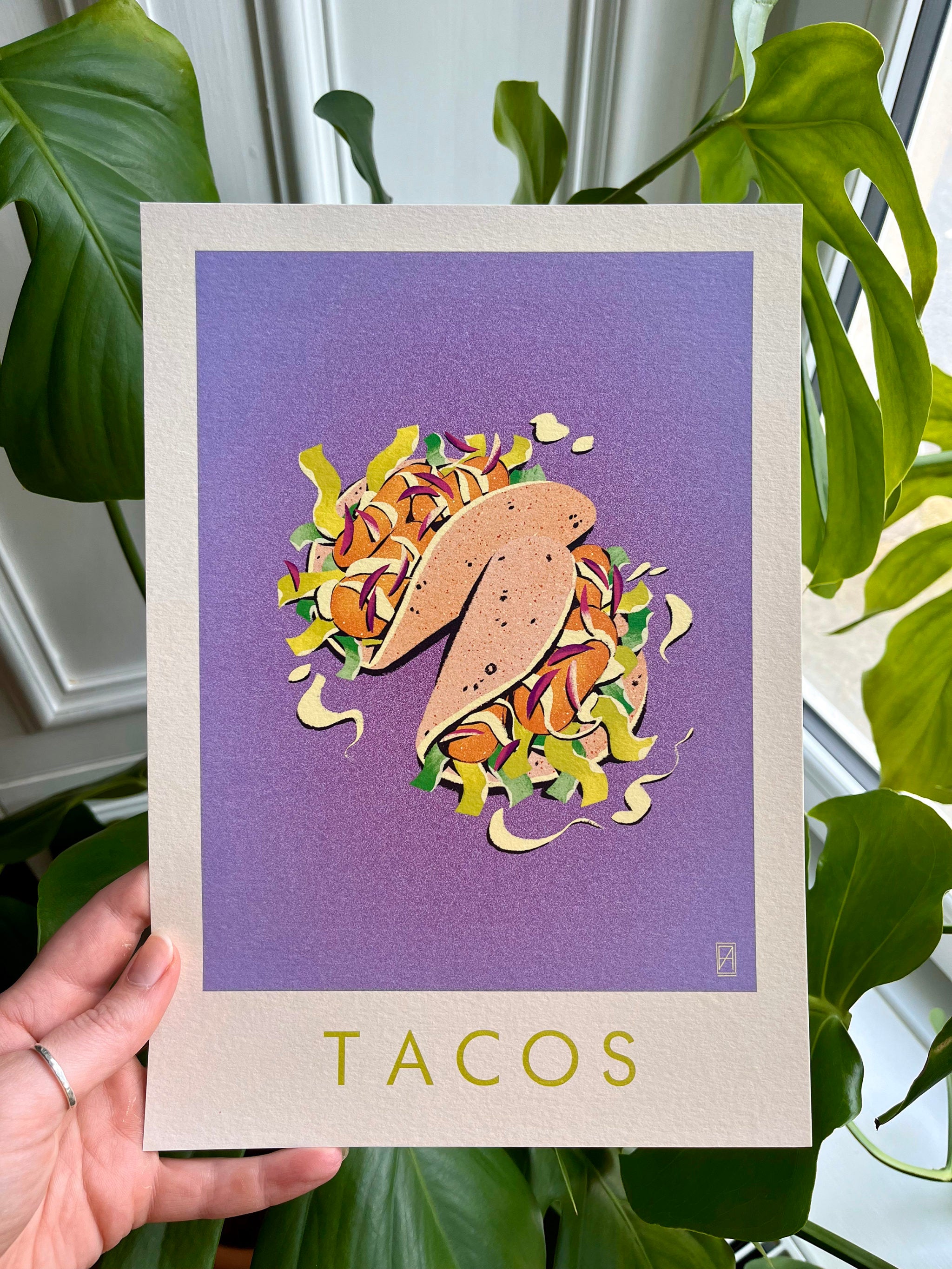 Taco print -- hand-held A4 card with a taco illustration on a purple background held in front of green plants.