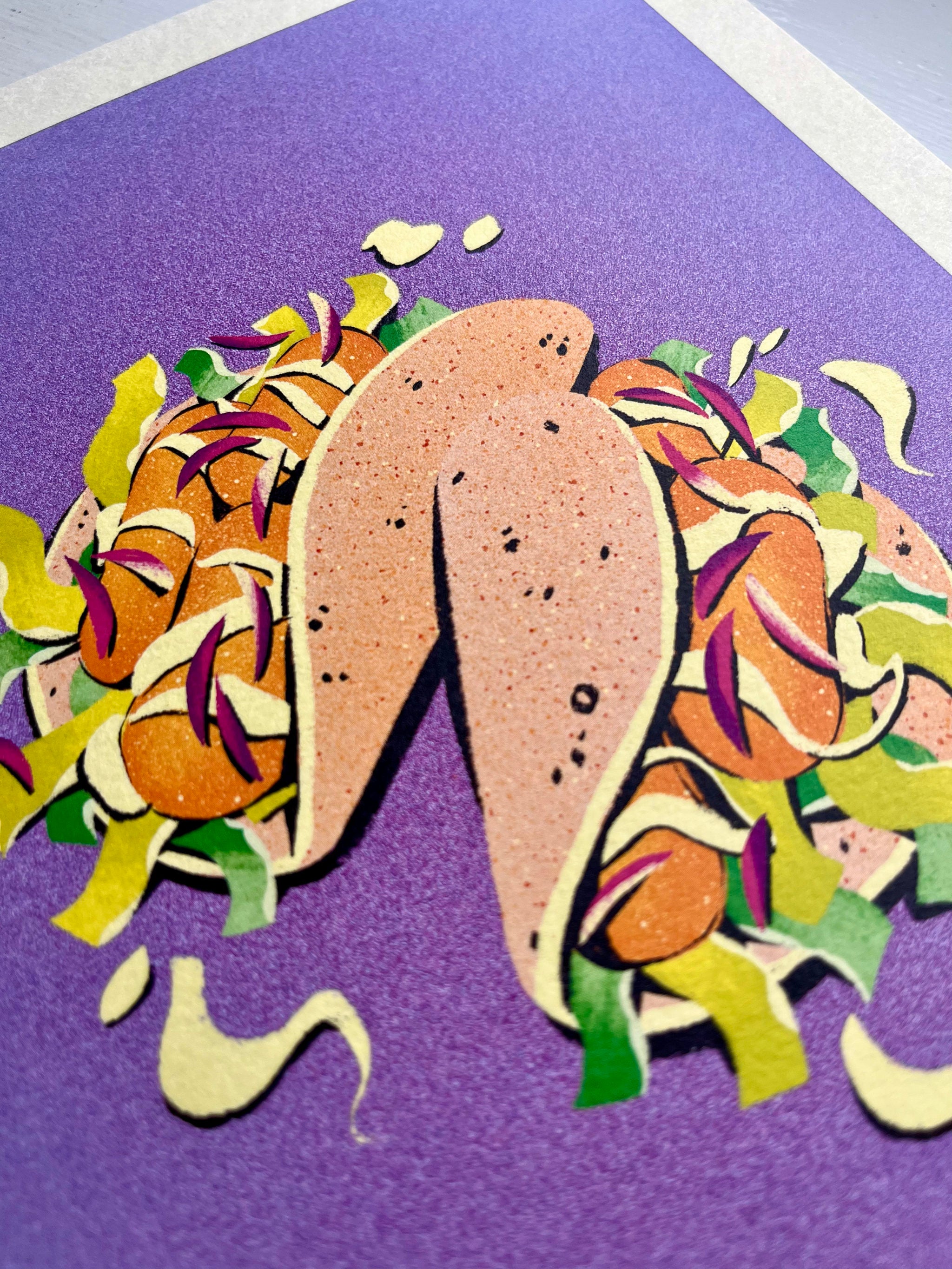 Taco print -- close-up of a colourful paper cutout of a taco with various toppings on a purple background.