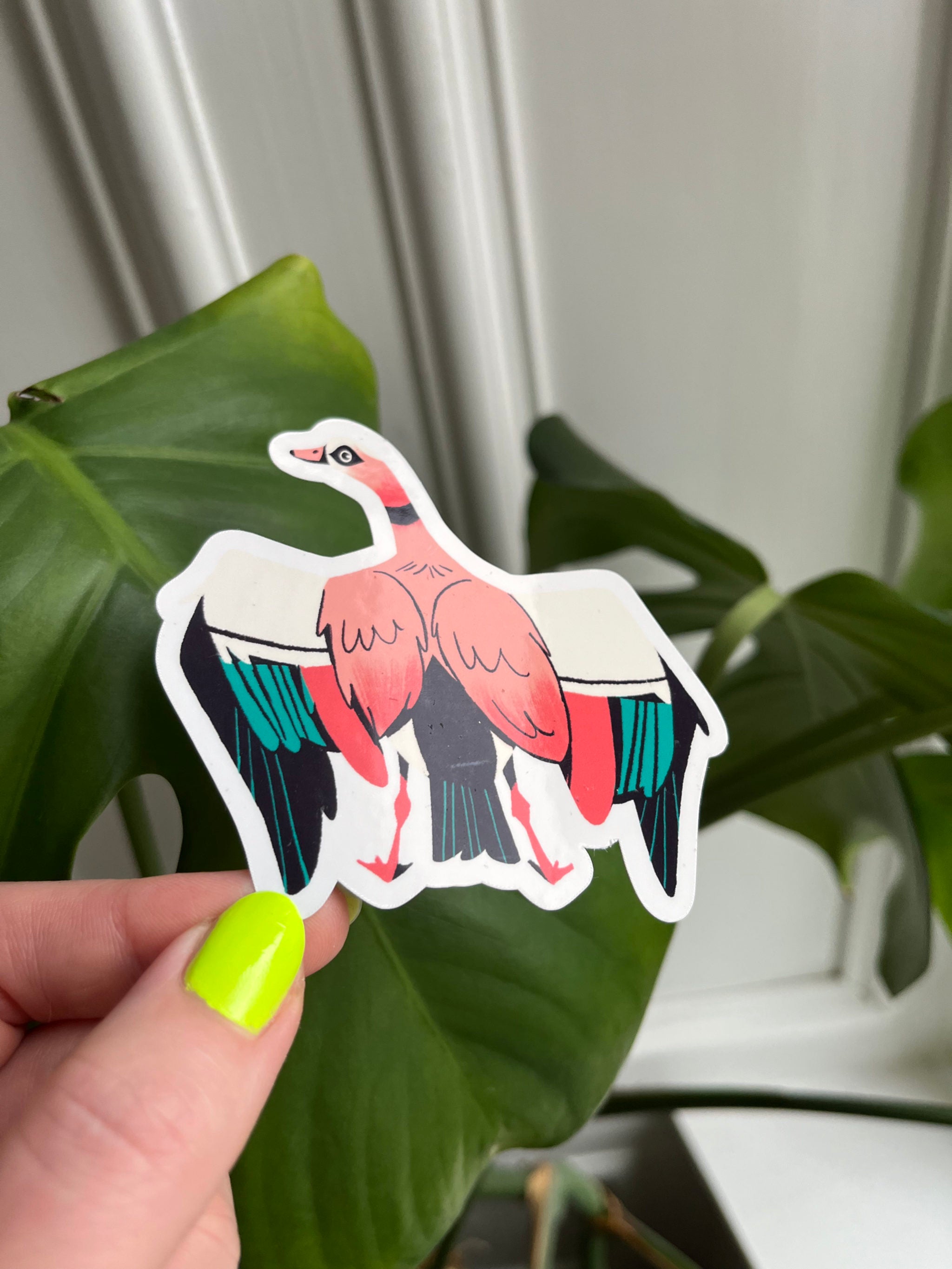Egyptian Goose sticker -- hand holding a colorful sticker of a bird against a green leafy background